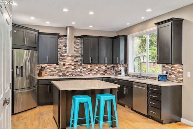 kitchen featuring light wood finished floors, light countertops, appliances with stainless steel finishes, wall chimney exhaust hood, and a sink