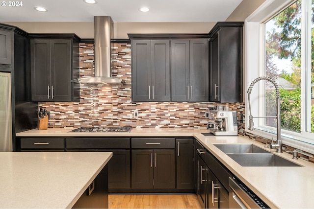 kitchen with stainless steel appliances, wall chimney exhaust hood, light countertops, and a sink