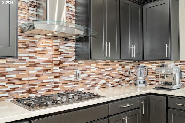 kitchen featuring light countertops, decorative backsplash, gray cabinets, stainless steel gas stovetop, and wall chimney exhaust hood