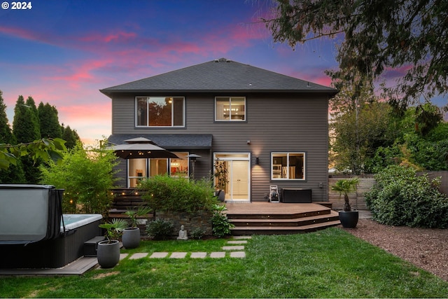 rear view of house with a yard, a shingled roof, a deck, and a hot tub