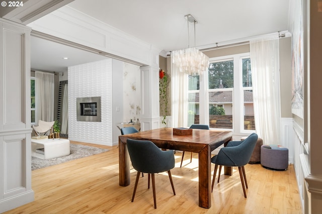 dining space with a decorative wall, decorative columns, light wood-style floors, and a chandelier