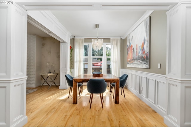 dining space featuring light wood finished floors, a chandelier, a wainscoted wall, decorative columns, and a decorative wall