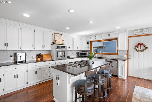 kitchen with a breakfast bar area, white cabinetry, appliances with stainless steel finishes, dark countertops, and dark wood finished floors