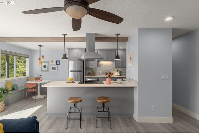 kitchen featuring island range hood, a peninsula, light countertops, freestanding refrigerator, and a kitchen bar