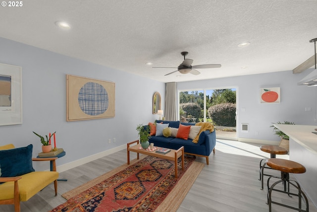 living area with light wood-type flooring, baseboards, a textured ceiling, and recessed lighting