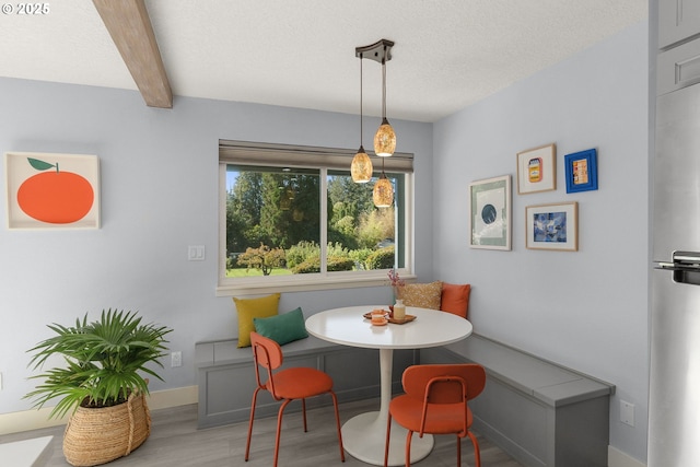 dining area with a textured ceiling, breakfast area, wood finished floors, baseboards, and beamed ceiling