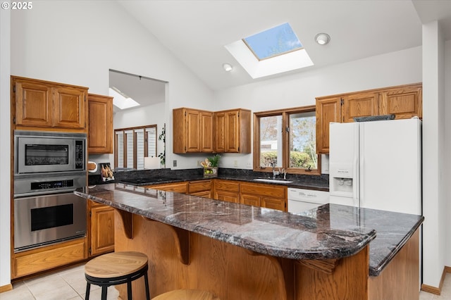 kitchen featuring light tile patterned floors, brown cabinetry, appliances with stainless steel finishes, a kitchen breakfast bar, and a sink