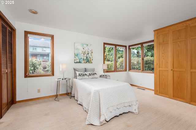 bedroom with light colored carpet, visible vents, baseboards, and multiple windows