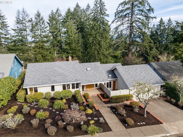 view of front of home featuring driveway, roof with shingles, and a chimney