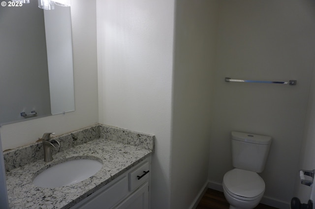 half bathroom with baseboards, vanity, and toilet