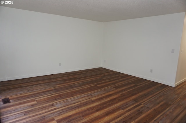 spare room with dark wood-style flooring, visible vents, a textured ceiling, and baseboards