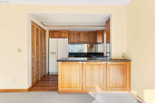 kitchen with white refrigerator with ice dispenser, kitchen peninsula, and dark stone countertops