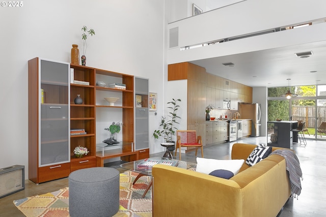 living area featuring visible vents, a ceiling fan, concrete floors, and a high ceiling