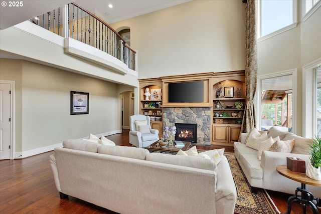 living room with a towering ceiling, a stone fireplace, dark wood-style floors, baseboards, and arched walkways
