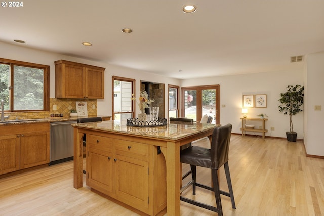 kitchen with a sink, visible vents, a center island, light stone countertops, and dishwasher