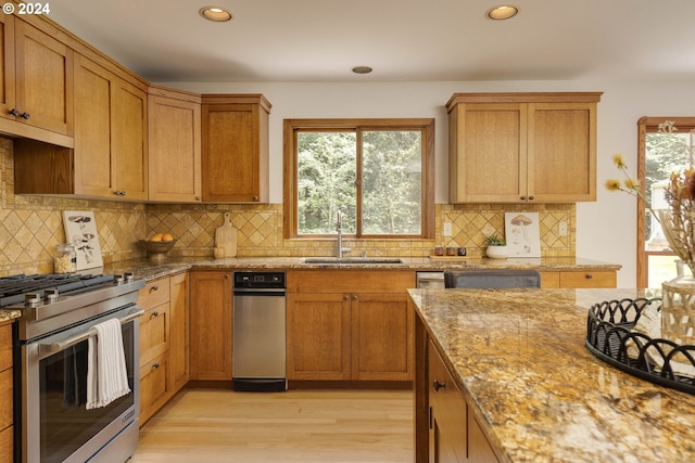 kitchen with light stone countertops, a sink, stainless steel range with gas cooktop, brown cabinets, and light wood finished floors