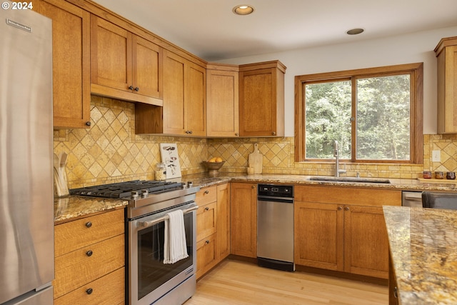 kitchen with light stone counters, stainless steel appliances, brown cabinetry, a sink, and light wood-type flooring