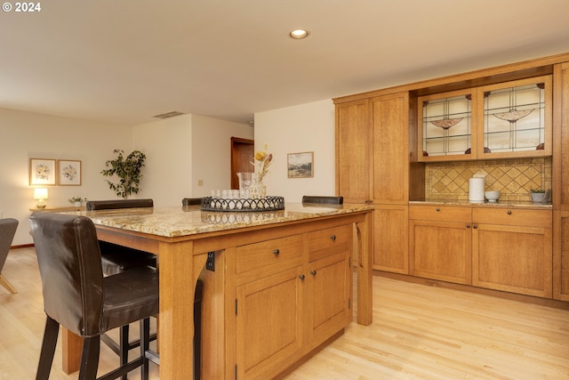 kitchen featuring a center island, brown cabinets, tasteful backsplash, light wood-style floors, and a kitchen breakfast bar