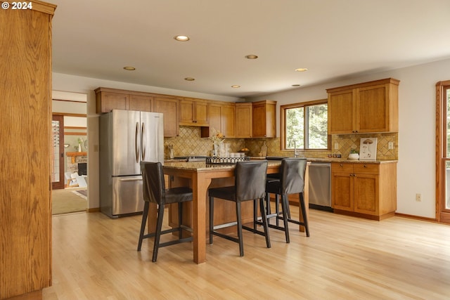 kitchen featuring brown cabinetry, light wood-style flooring, appliances with stainless steel finishes, a breakfast bar, and a center island