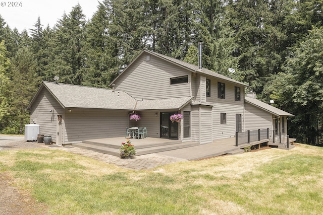 rear view of property featuring a shingled roof, central AC unit, a deck, and a lawn