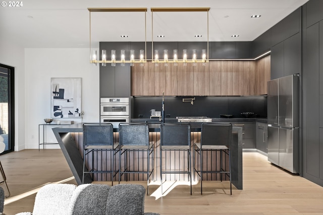 kitchen with hanging light fixtures, an island with sink, a kitchen bar, appliances with stainless steel finishes, and light wood-type flooring