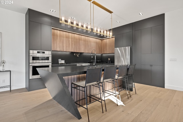 kitchen with pendant lighting, light wood-type flooring, a kitchen island with sink, a breakfast bar, and appliances with stainless steel finishes