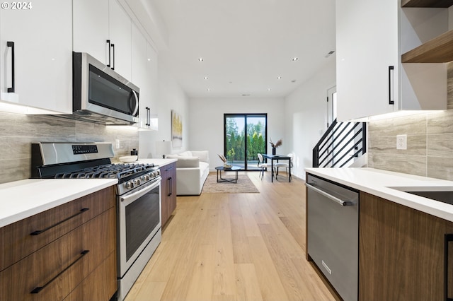 kitchen featuring white cabinetry, decorative backsplash, dark brown cabinets, appliances with stainless steel finishes, and light wood-type flooring