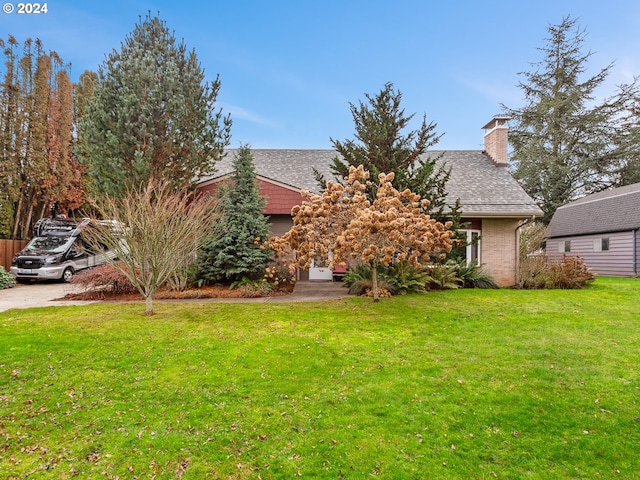 view of property hidden behind natural elements featuring an outbuilding, roof with shingles, and a front yard