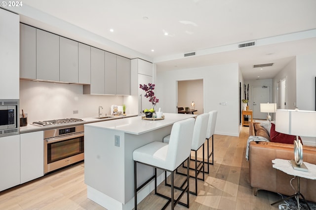 kitchen featuring a sink, stainless steel appliances, a kitchen bar, modern cabinets, and light wood-type flooring