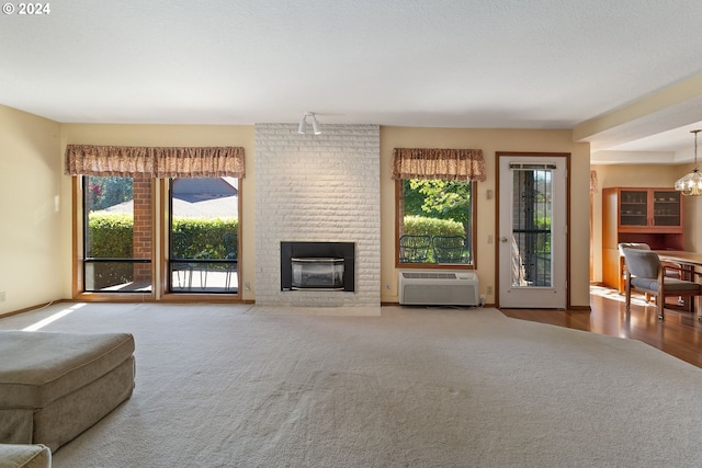 unfurnished living room featuring a wall unit AC, a fireplace, hardwood / wood-style floors, a notable chandelier, and a textured ceiling