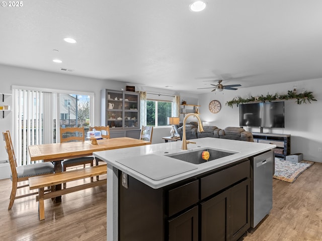 kitchen with sink, stainless steel dishwasher, ceiling fan, light wood-type flooring, and an island with sink