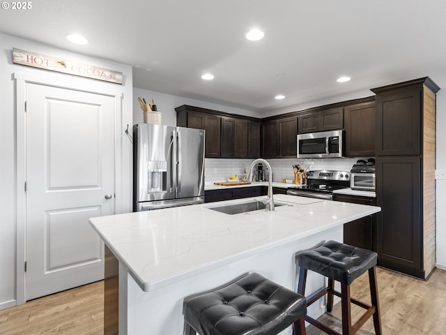 kitchen with sink, an island with sink, a breakfast bar area, appliances with stainless steel finishes, and light wood-type flooring