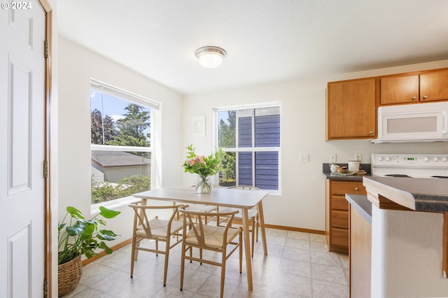 kitchen with white microwave, baseboards, range, light floors, and dark countertops