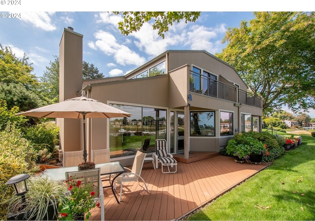 rear view of property with a balcony, a yard, and a wooden deck