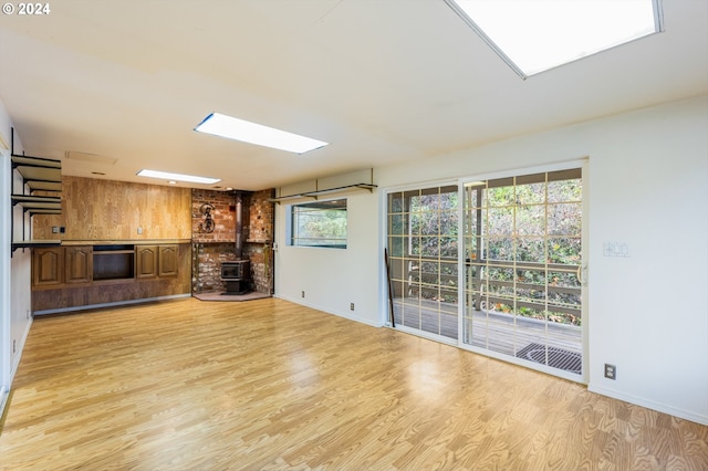 unfurnished living room with light wood-type flooring, wooden walls, and a wood stove