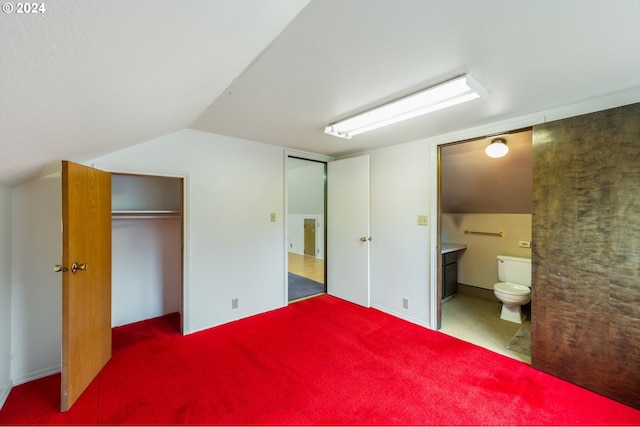 unfurnished bedroom with dark colored carpet, ensuite bath, a closet, and lofted ceiling