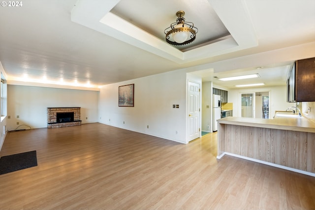 unfurnished living room with a stone fireplace, a raised ceiling, light wood-type flooring, and sink