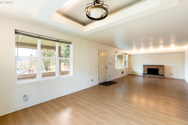 unfurnished living room with a fireplace, light wood-type flooring, and a tray ceiling