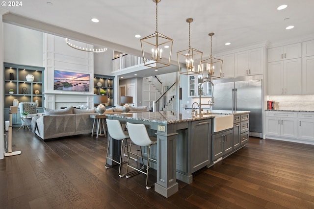 kitchen featuring white cabinetry, hanging light fixtures, dark wood-type flooring, stainless steel built in refrigerator, and a kitchen island with sink