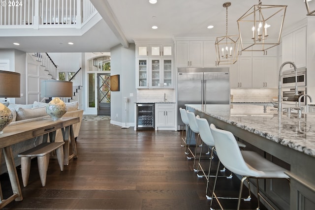 kitchen with tasteful backsplash, beverage cooler, dark wood-type flooring, white cabinetry, and hanging light fixtures