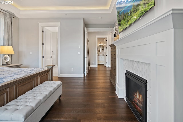 bedroom with dark hardwood / wood-style flooring, a tile fireplace, and a tray ceiling