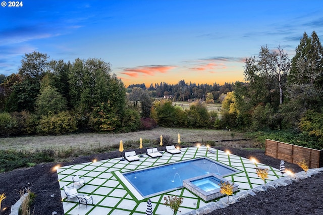 pool at dusk featuring an in ground hot tub and pool water feature