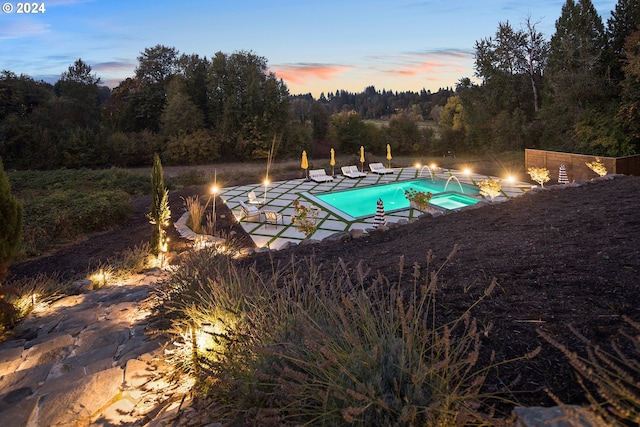 pool at dusk featuring an in ground hot tub and a patio