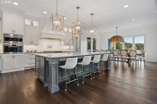 kitchen featuring a center island with sink, dark hardwood / wood-style flooring, white cabinetry, and hanging light fixtures