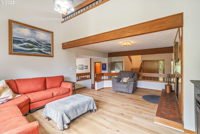 living room featuring stairs, beam ceiling, a fireplace, wood finished floors, and a textured ceiling