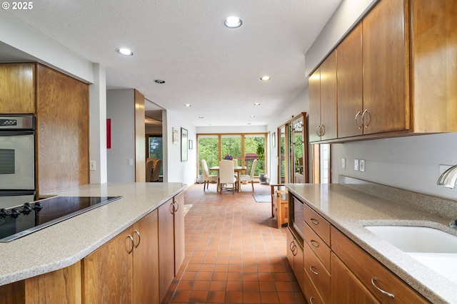 kitchen with oven, brown cabinets, a sink, recessed lighting, and black electric cooktop