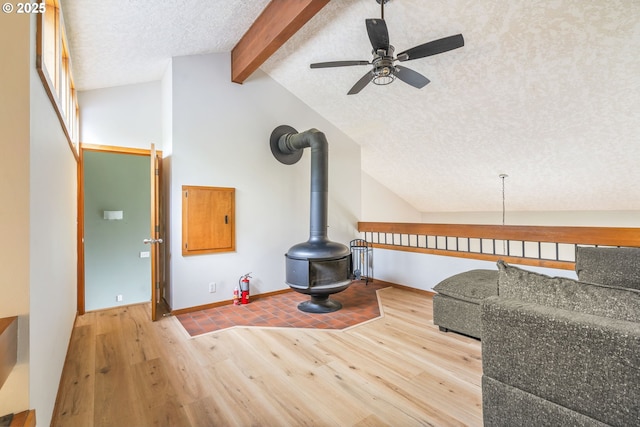 living room with lofted ceiling with beams, a wood stove, wood finished floors, a textured ceiling, and a ceiling fan