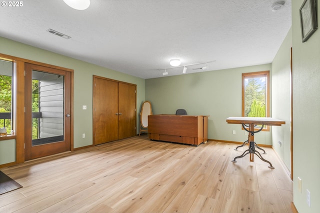 home office featuring light wood finished floors, track lighting, and a textured ceiling