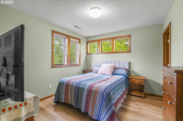 bedroom with light wood-type flooring, visible vents, baseboards, and a textured ceiling