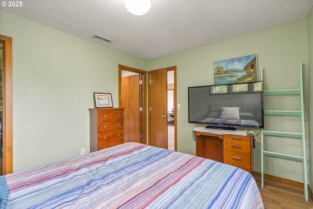 bedroom with wood finished floors, visible vents, and a textured ceiling